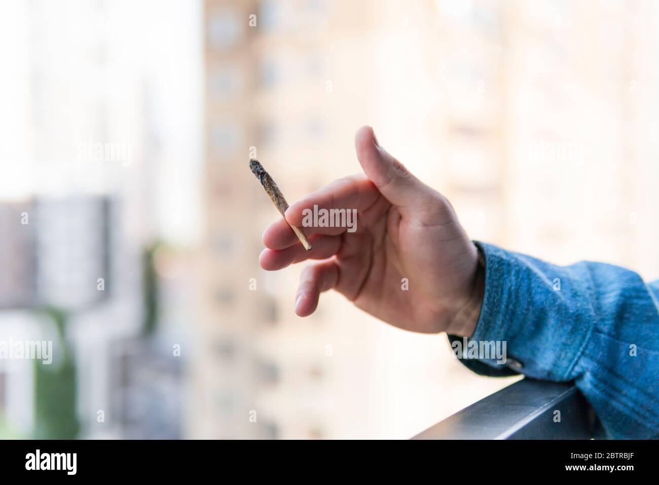 Primo piano di presa di mano maschile e fumare marijuana comune o sigaretta all'aperto. La cannabis è un concetto di medicina alternativa e a base di erbe Foto Stock