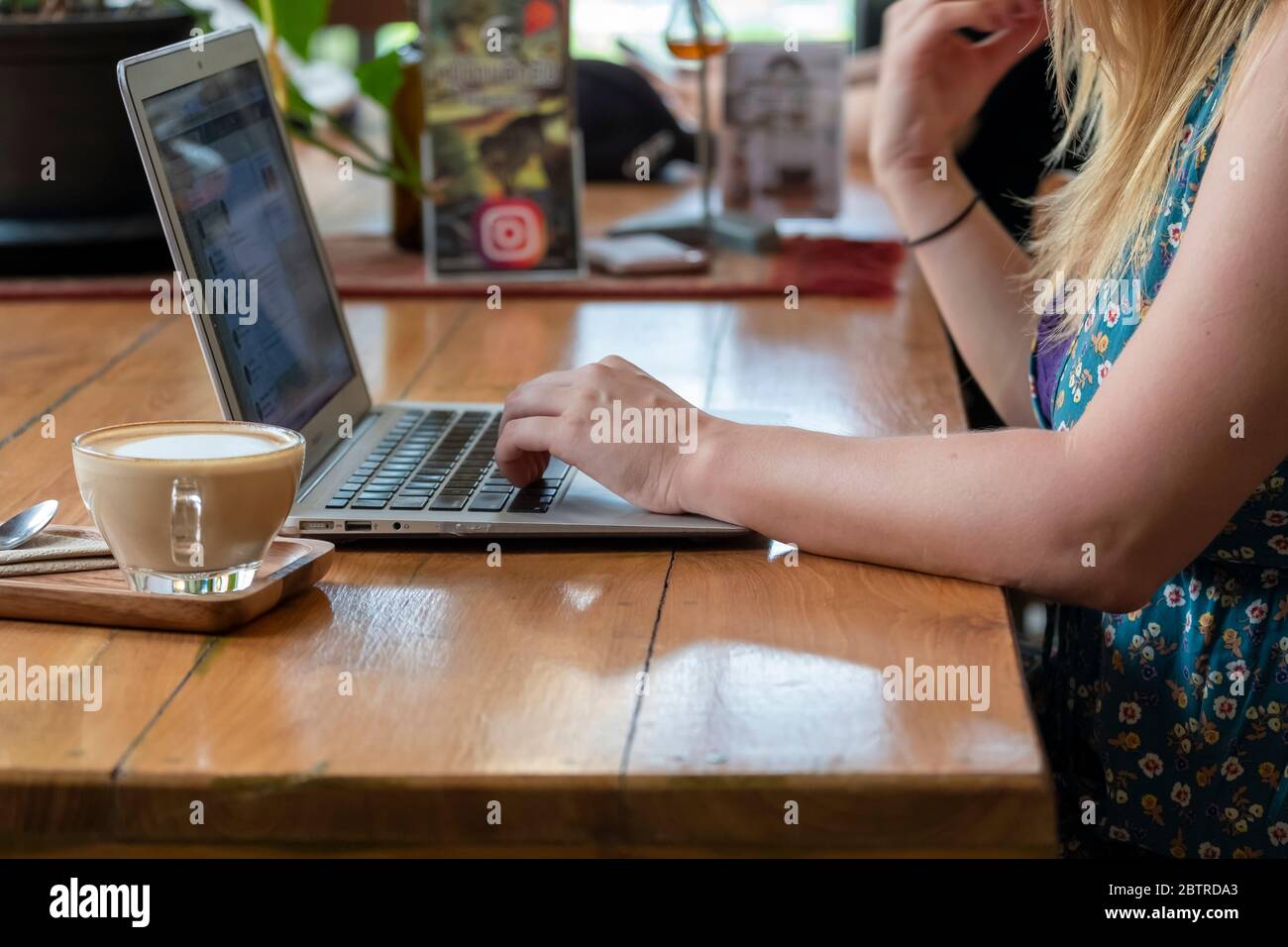 Una donna che lavora su un computer portatile, con una tazza di caffè in un ufficio domestico o in un caffè Foto Stock