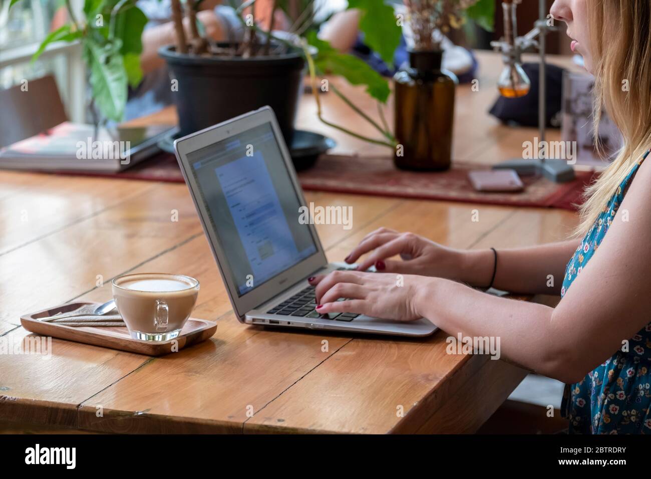 Una donna che lavora su un computer portatile, con una tazza di caffè in un ufficio domestico o in un caffè Foto Stock