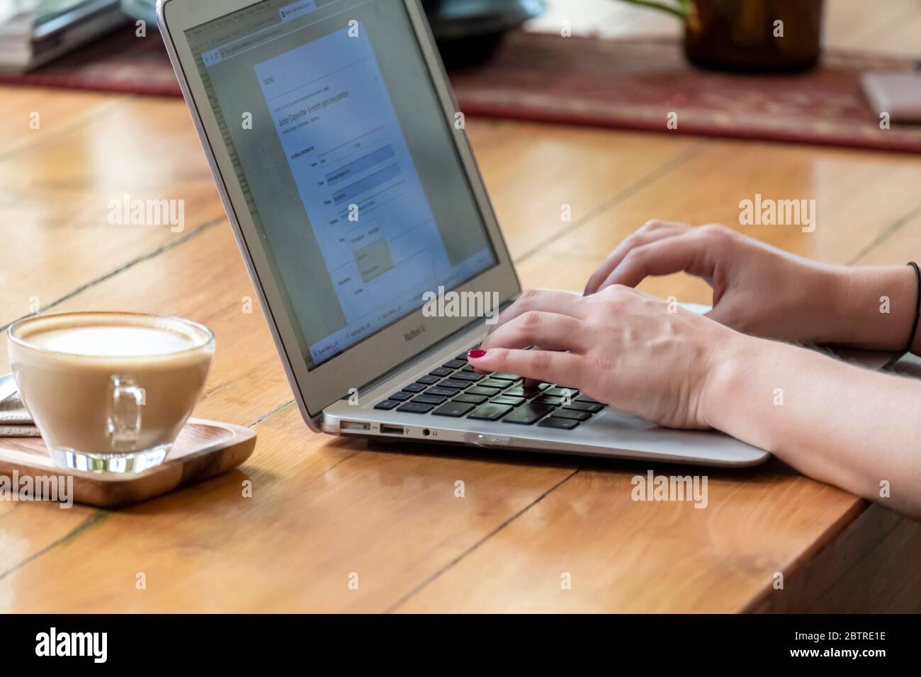 Una donna che lavora su un computer portatile, con una tazza di caffè in un ufficio domestico o in un caffè Foto Stock