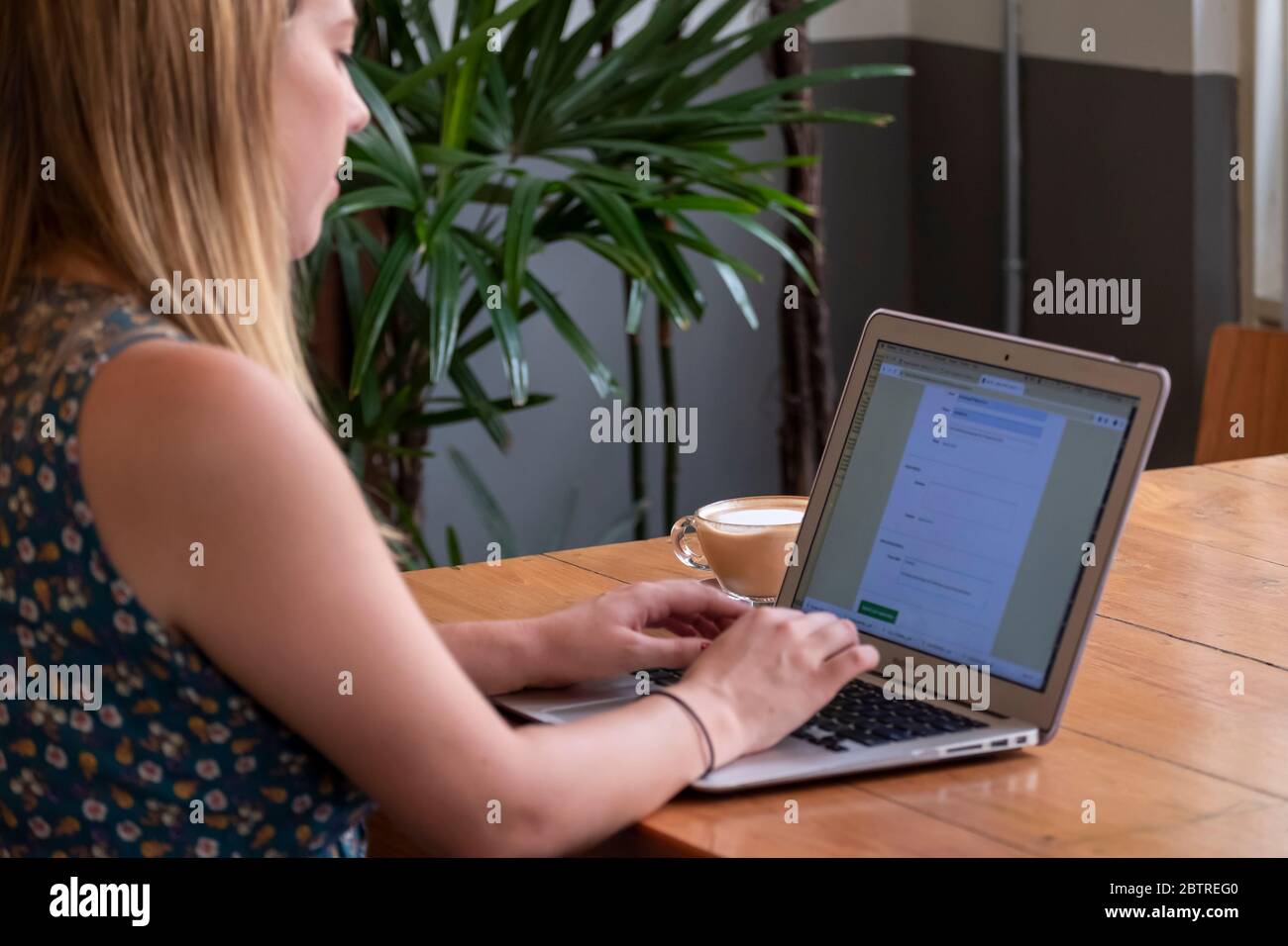 Una donna che lavora su un computer portatile, con una tazza di caffè in un ufficio domestico o in un caffè Foto Stock
