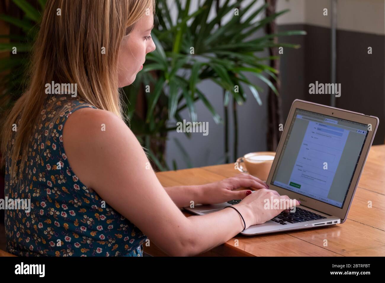 Una donna che lavora su un computer portatile, con una tazza di caffè in un ufficio domestico o in un caffè Foto Stock