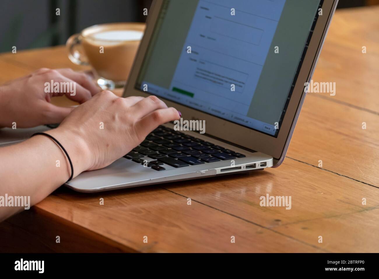 Una donna che lavora su un computer portatile, con una tazza di caffè in un ufficio domestico o in un caffè Foto Stock