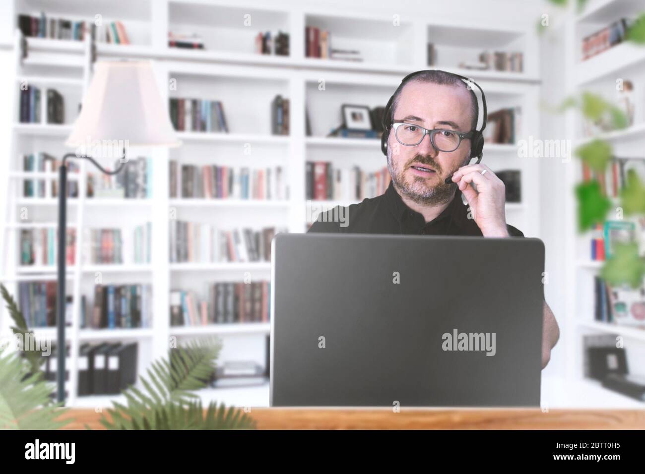 Uomo adulto che lavora a casa sul suo laptop con gli auricolari mentre partecipa a una riunione di squadra online. Concetto di autoisolamento e telelavoro. Spazio di copia Foto Stock