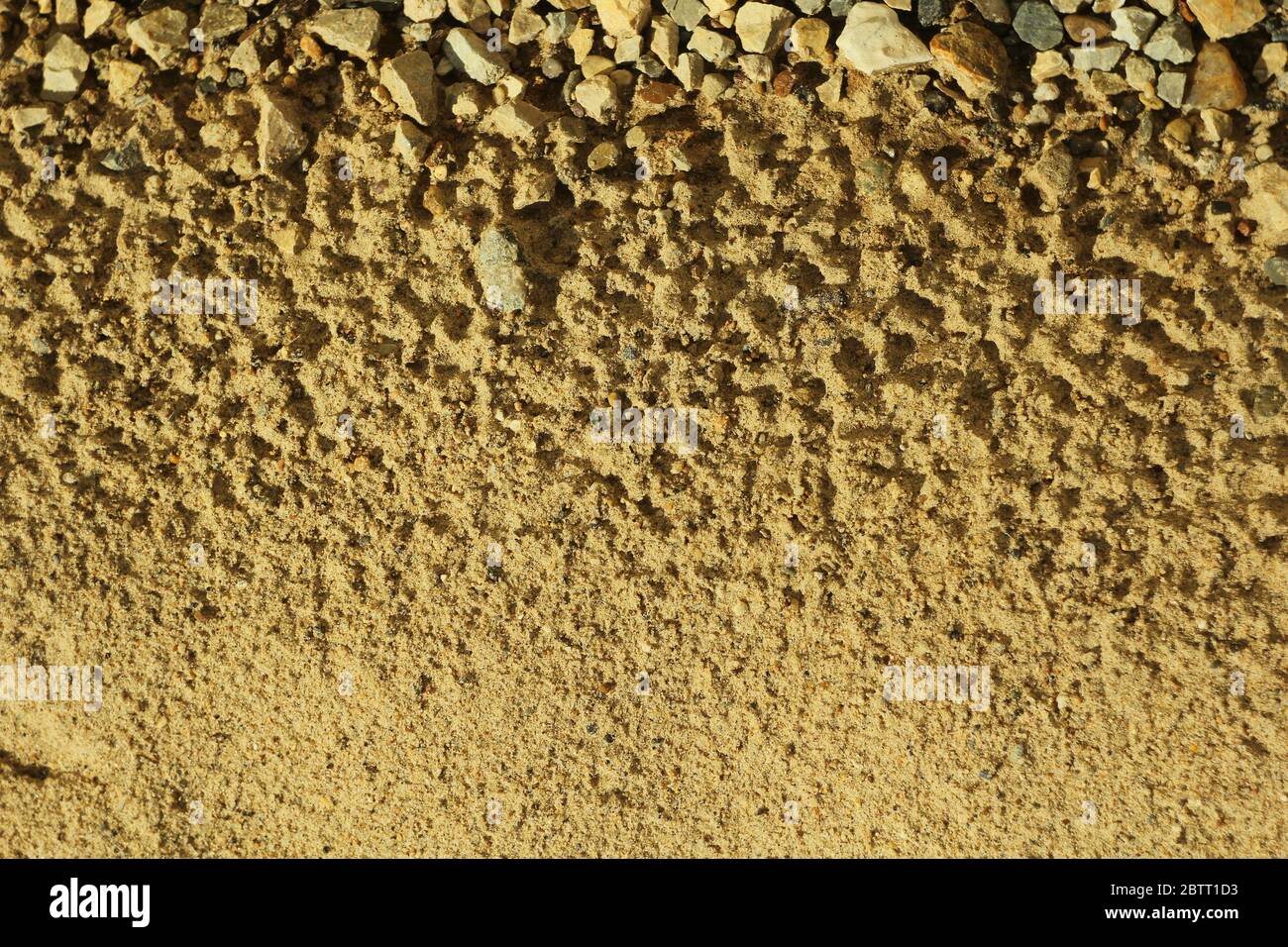Sabbia con tracce di gocce d'acqua e piccole pietre. Spiaggia sul mare. La consistenza della sabbia, illuminata dal sole. Posiziona testo e sfondo per la progettazione. Foto Stock