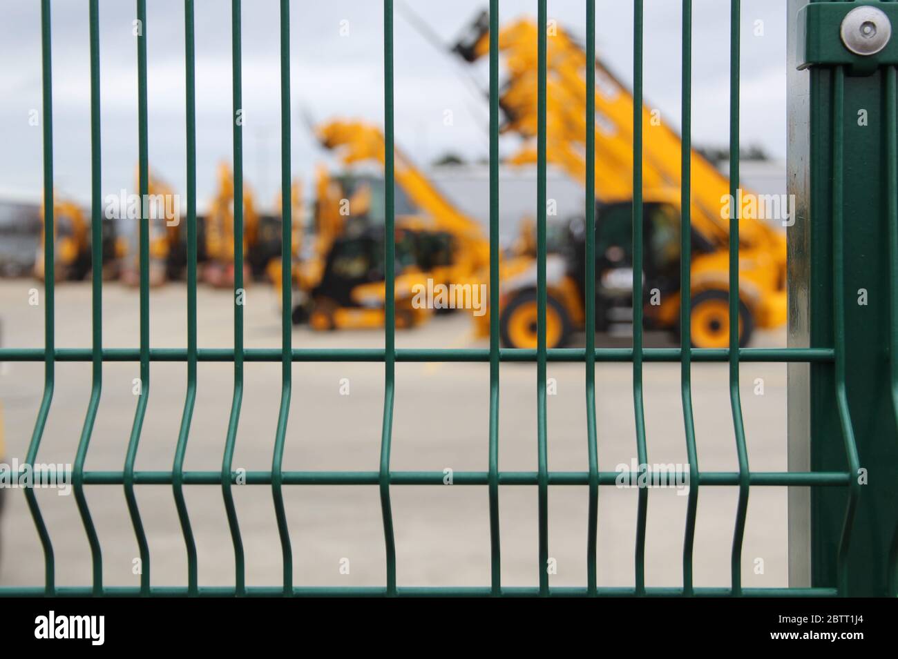 Flotta di veicoli Yellow Construction dietro una fence Foto Stock