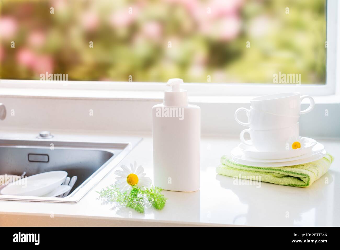 Detergente ecologico atossico con ingredienti naturali, fiori di camomilla, tazze bianche pulite e piastre vicino al lavandino con piatto sporco. Cura della pelle Foto Stock
