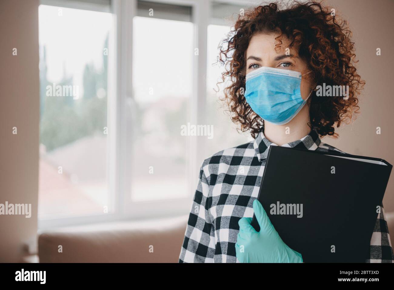 Affascinante medico caucasico con capelli ricci che tengono alcuni documenti e indossando maschera N95 viso con guanti Foto Stock