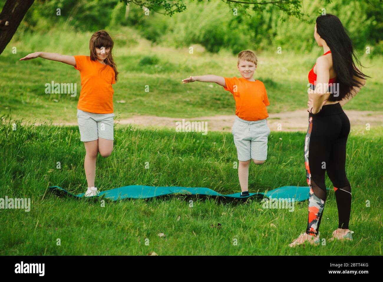 Il coach aiuta i bambini a completare l'esercizio. Fai sport all'aperto. Concetto di stile di vita sano. Baby yoga, allenamento fitness. Foto Stock