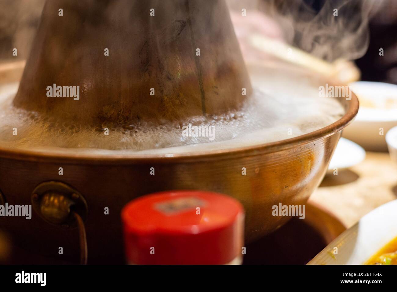 Tradizionale Beijing stile cinese carbone-riscaldato pentola con una ciambella di ottone a forma di ciambella. Posto al centro del tavolo da pranzo, ingredienti freschi e crudi Foto Stock