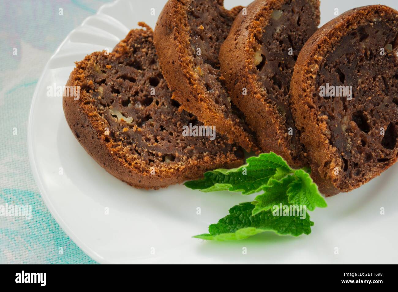 Pezzi di torta al cioccolato su un piatto bianco decorato con la menta da vicino su uno sfondo di tovagliolo colorato Foto Stock