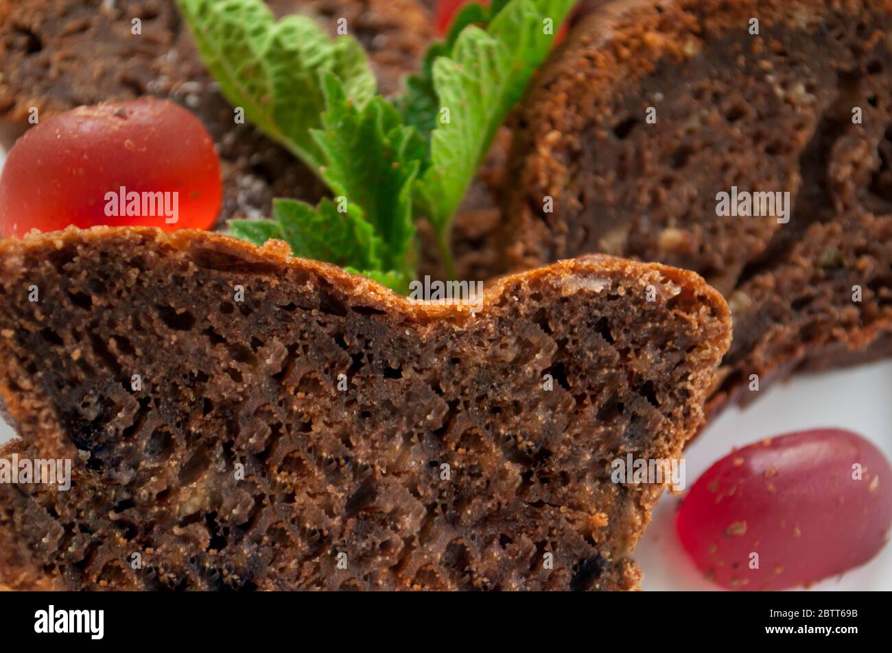 Pezzi di torta al cioccolato e caramelle di gelatina rossa su un piatto bianco decorato con primo piano di menta Foto Stock