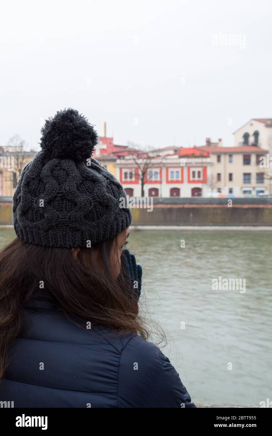 Immagine verticale della donna delle bruna che guarda al fiume Adige durante la fredda giornata a Verona Foto Stock