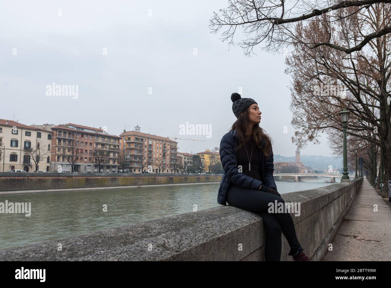 Immagine orizzontale della donna delle bruna che si posa sul fiume Adige durante la fredda giornata a Verona Foto Stock