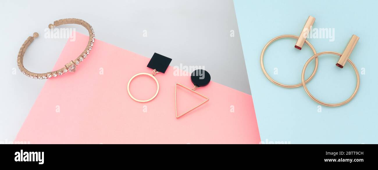 Posa piatta di moderni orecchini geometrici e bracciale in oro su carta rosa e blu Foto Stock