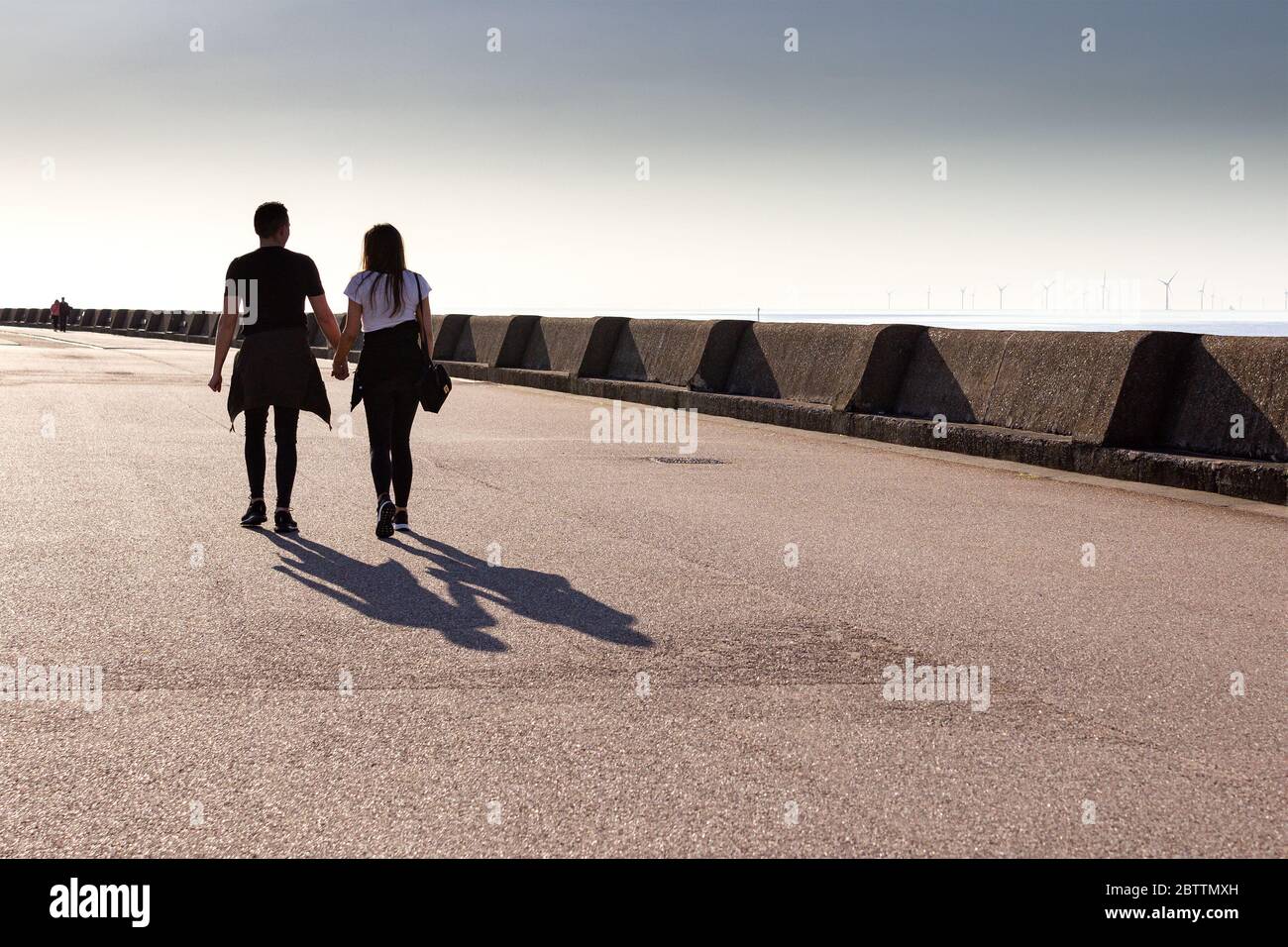 Silhouette di coppia che cammina sulla passeggiata in tarda serata sole, lunghe ombre, New Brighton. Foto Stock