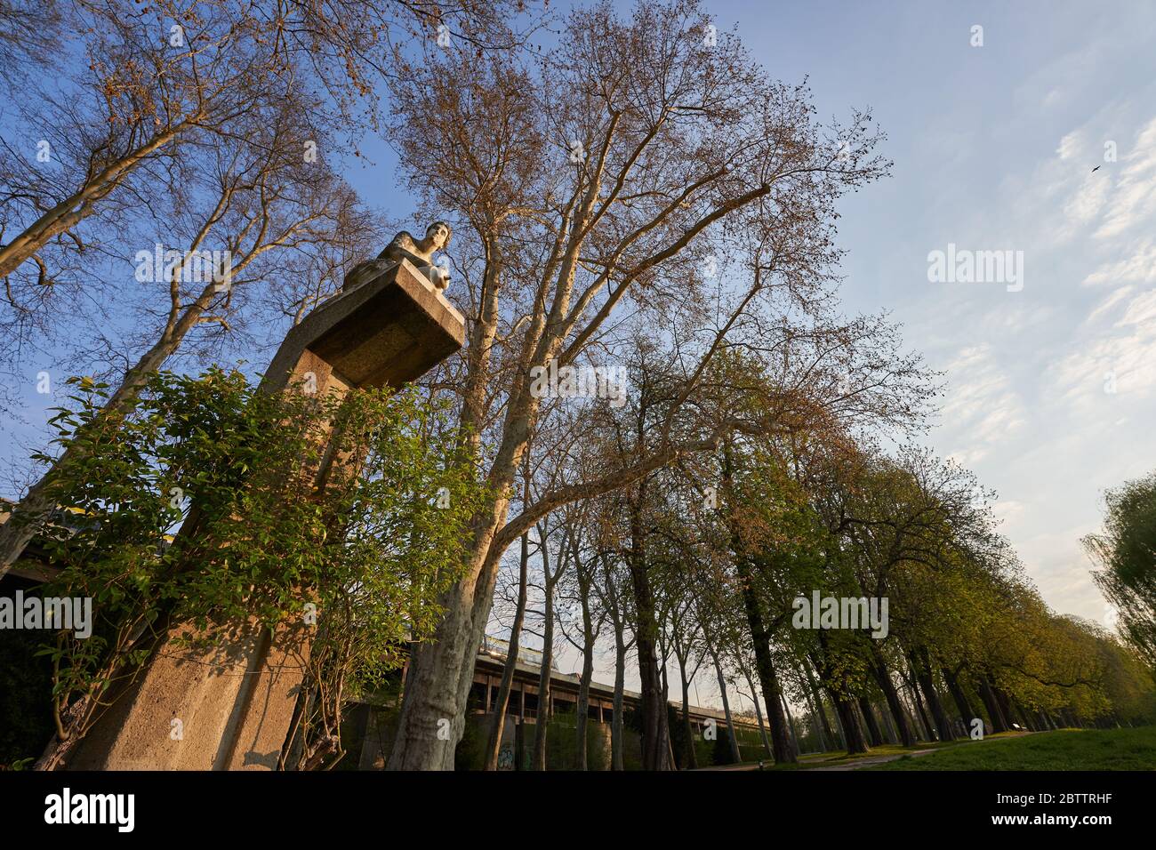 La statua in pietra si inginocchia sul piedistallo alto e contiene vasetto di argilla appena visibile, fotografato in modo ripido verso l'alto con Weit Winkel, im Rosenstein Park Foto Stock