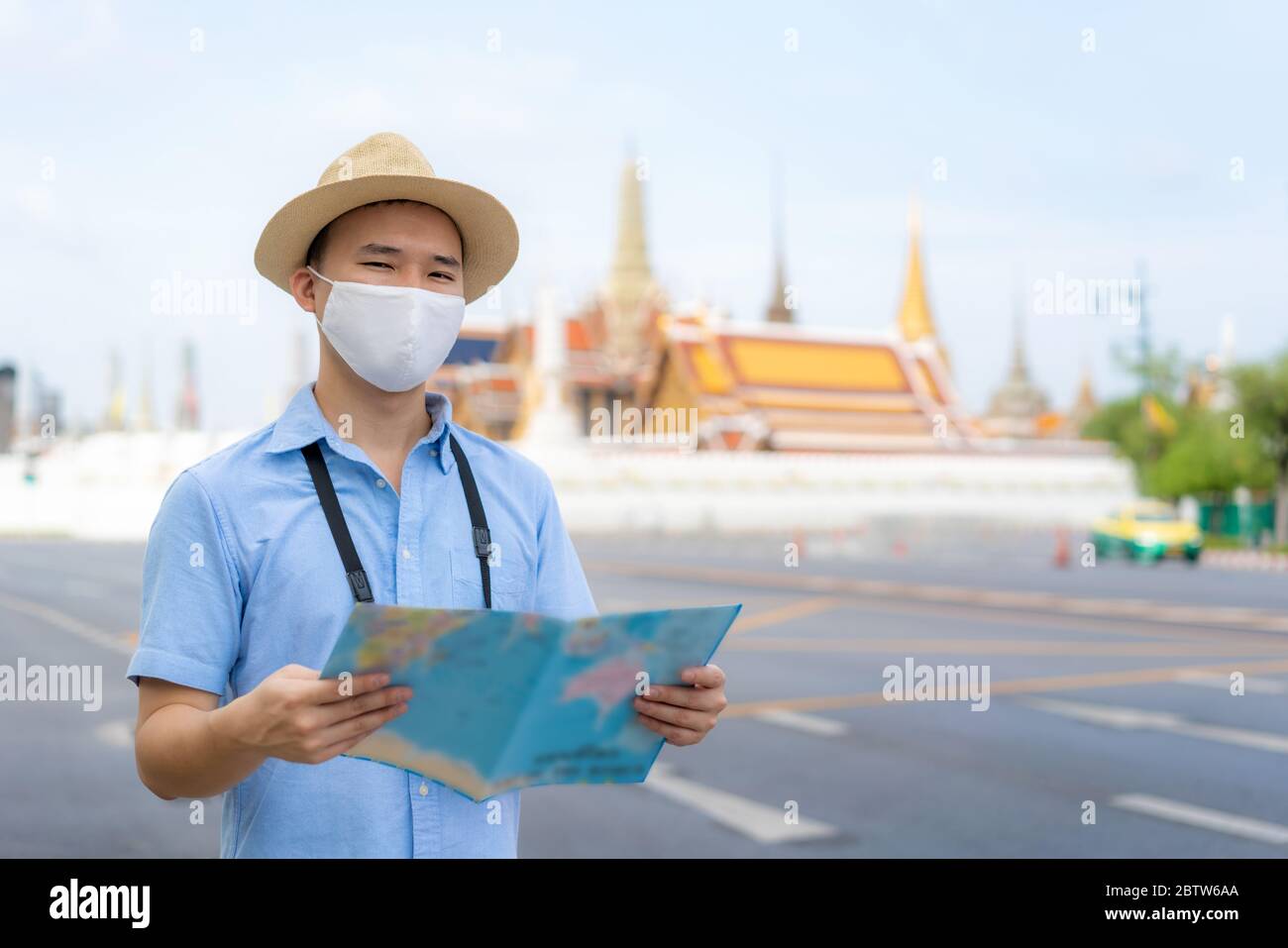 Uomo asiatico turisti felici di viaggiare indossando maschera per proteggere da Covid-19 sulle sue vacanze e lui guardando la mappa di viaggio nel tempio Wat Phra Kaew a Bangk Foto Stock