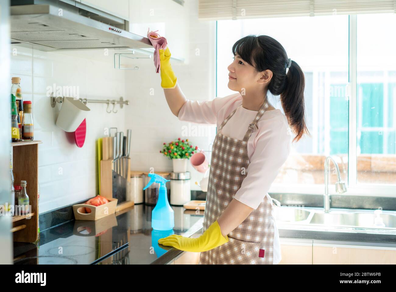 Donna asiatica che indossa guanti di gomma protettiva cucina di pulizia cappa di cottura a casa sua durante il soggiorno a casa utilizzando il tempo libero circa la loro casa quotidiana Foto Stock