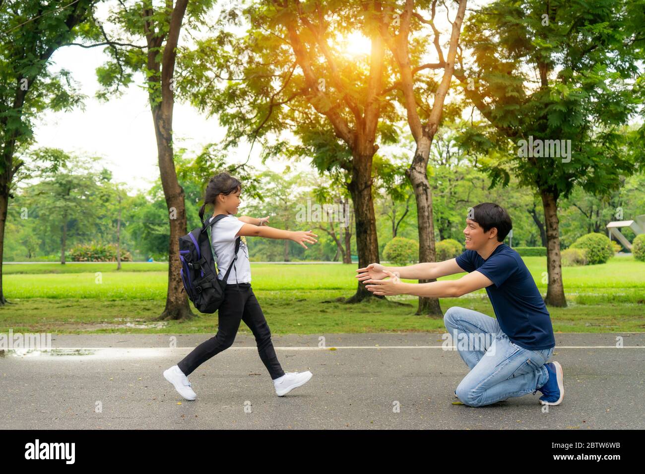 Una studentessa asiatica di scuola materna che corre nelle mani del padre per abbracciarla dopo essere tornata a scuola di fronte a casa nel villaggio. Genitorialità o amore e legame Foto Stock
