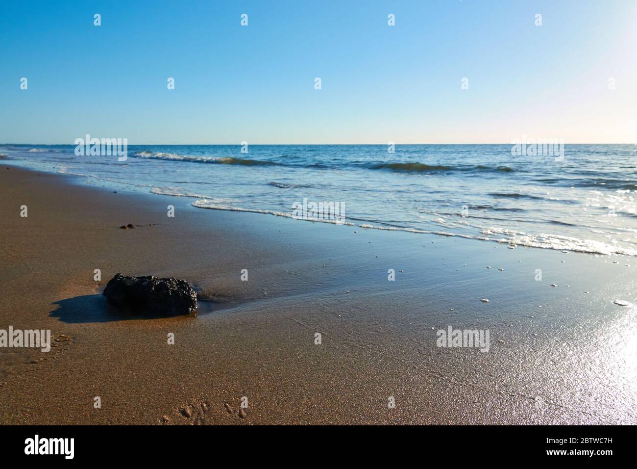Pietra singola sulla spiaggia di sabbia di fronte all'oceano. Cielo blu. Spazio per fotocopie. Foto Stock