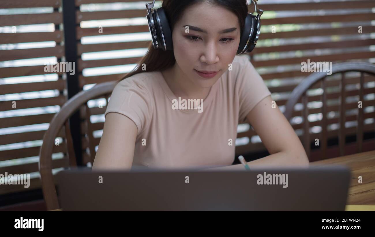 Una giovane studentessa seduto al tavolo, utilizzando un computer portatile quando studia online a casa Foto Stock