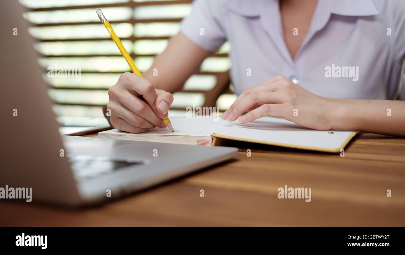 Nota di scrittura della ragazza giovane con l'elenco delle idee ispirate della penna sul blocco note mentre lavora sul computer portatile Foto Stock