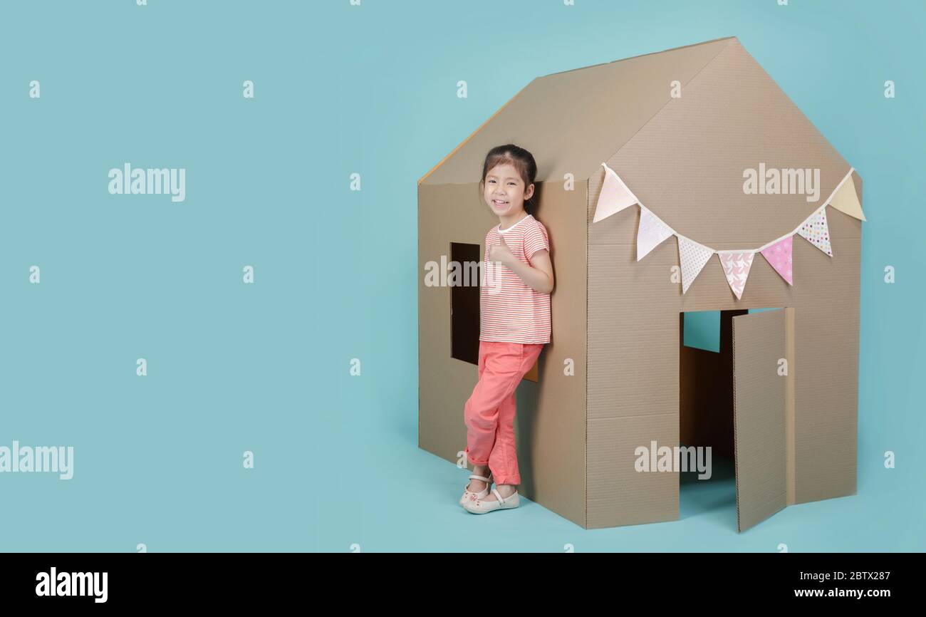 Ragazza bambino asiatica giocare con casa di cartone isolato su banner blu lungo con spazio di copia per il tuo testo, Creative a casa con concetto di famiglia Foto Stock