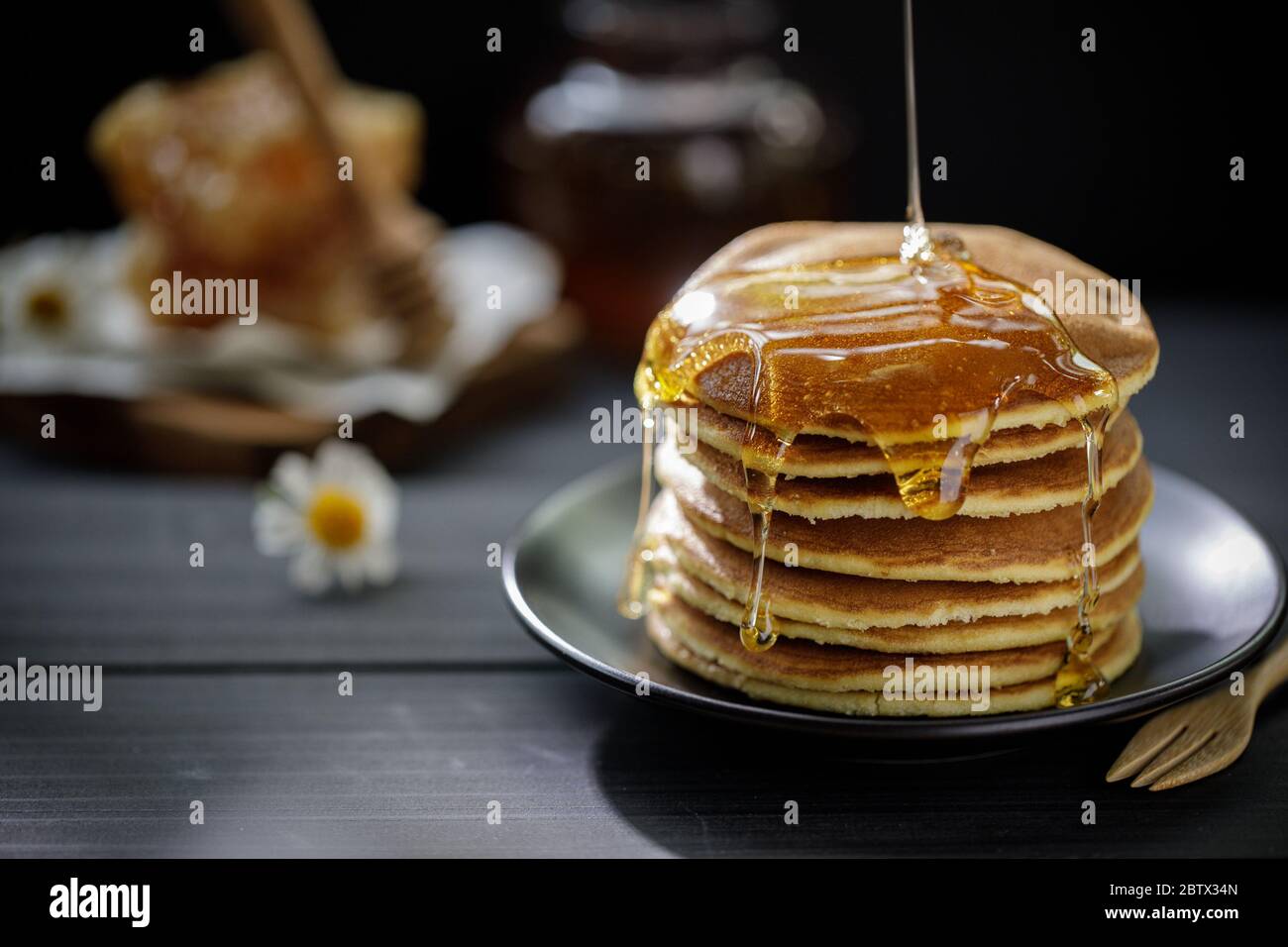 Il miele gocciola sulla pila di frittelle per la colazione sul tavolo di legno, prodotti sani dal concetto di ingredienti naturali biologici Foto Stock