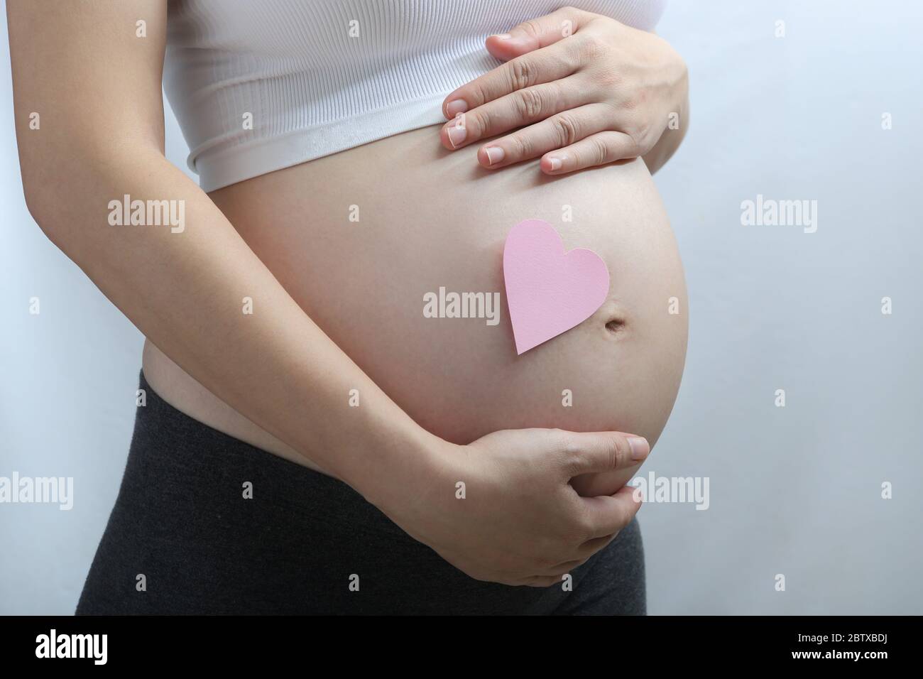 la donna incinta con camicia bianca è prenderlo cura del suo bambino con una carta di nota sul suo stomaco. Foto Stock