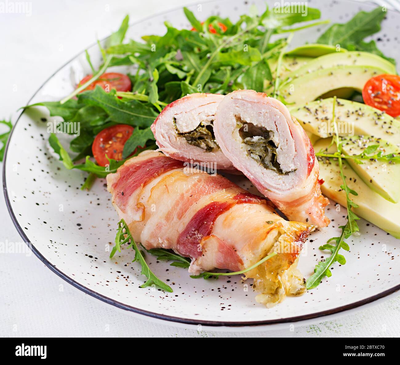 Dieta chetogena. Piatto per cena con involtino di carne di pollo, pancetta, avocado, pomodori e rucola. Disintossicazione e concetto sano. Keto alimentare. Foto Stock