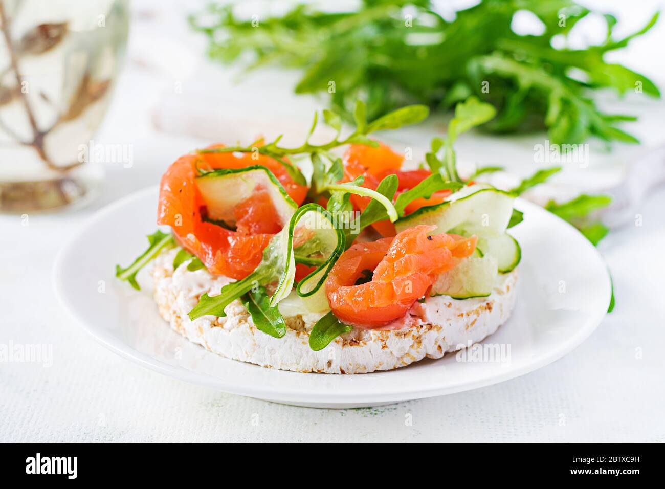 Sandwich aperto con salmone salato con croccante, formaggio spalmabile, cetriolo a fette e rucola sul piatto. Foto Stock