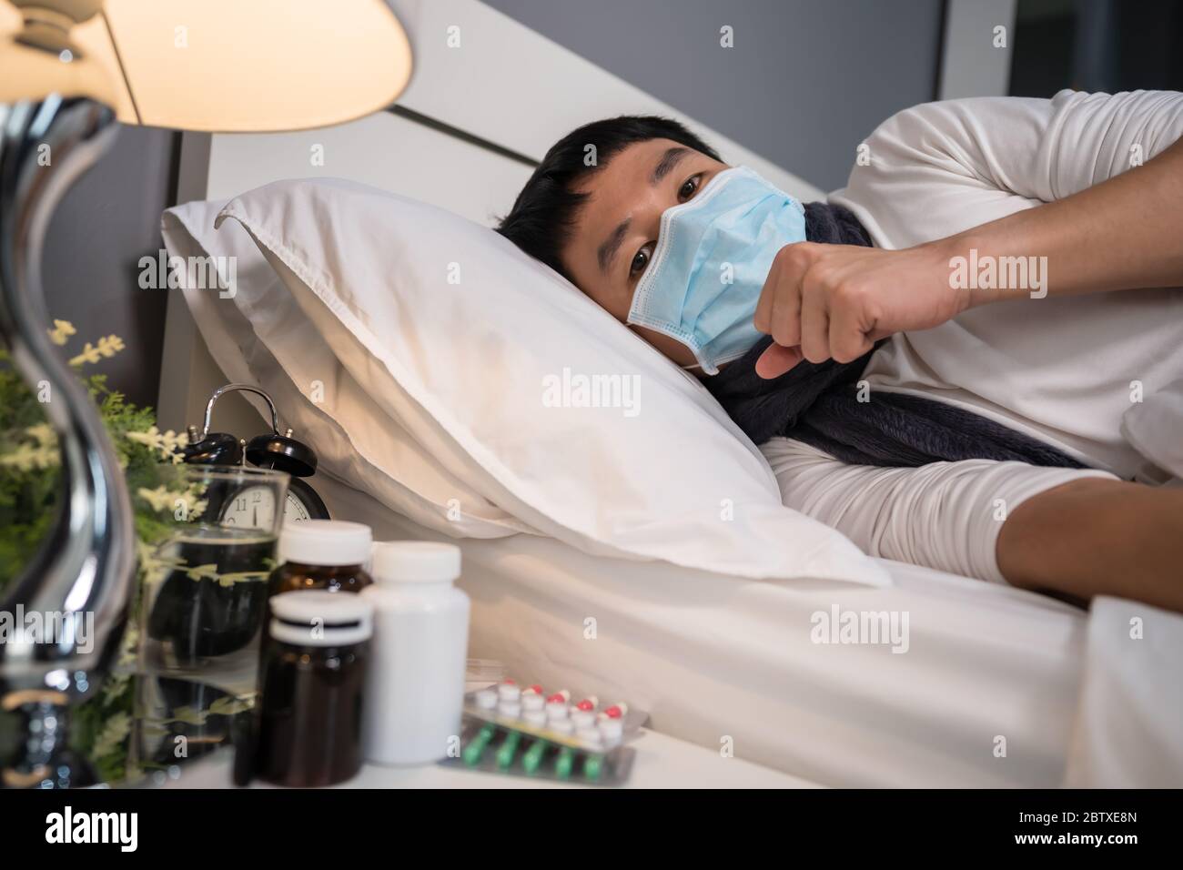 malato uomo in maschera medica tosse e sofferente di malattia virale e febbre in un letto, coronavirus (covid-19) concetto pandemico. Foto Stock