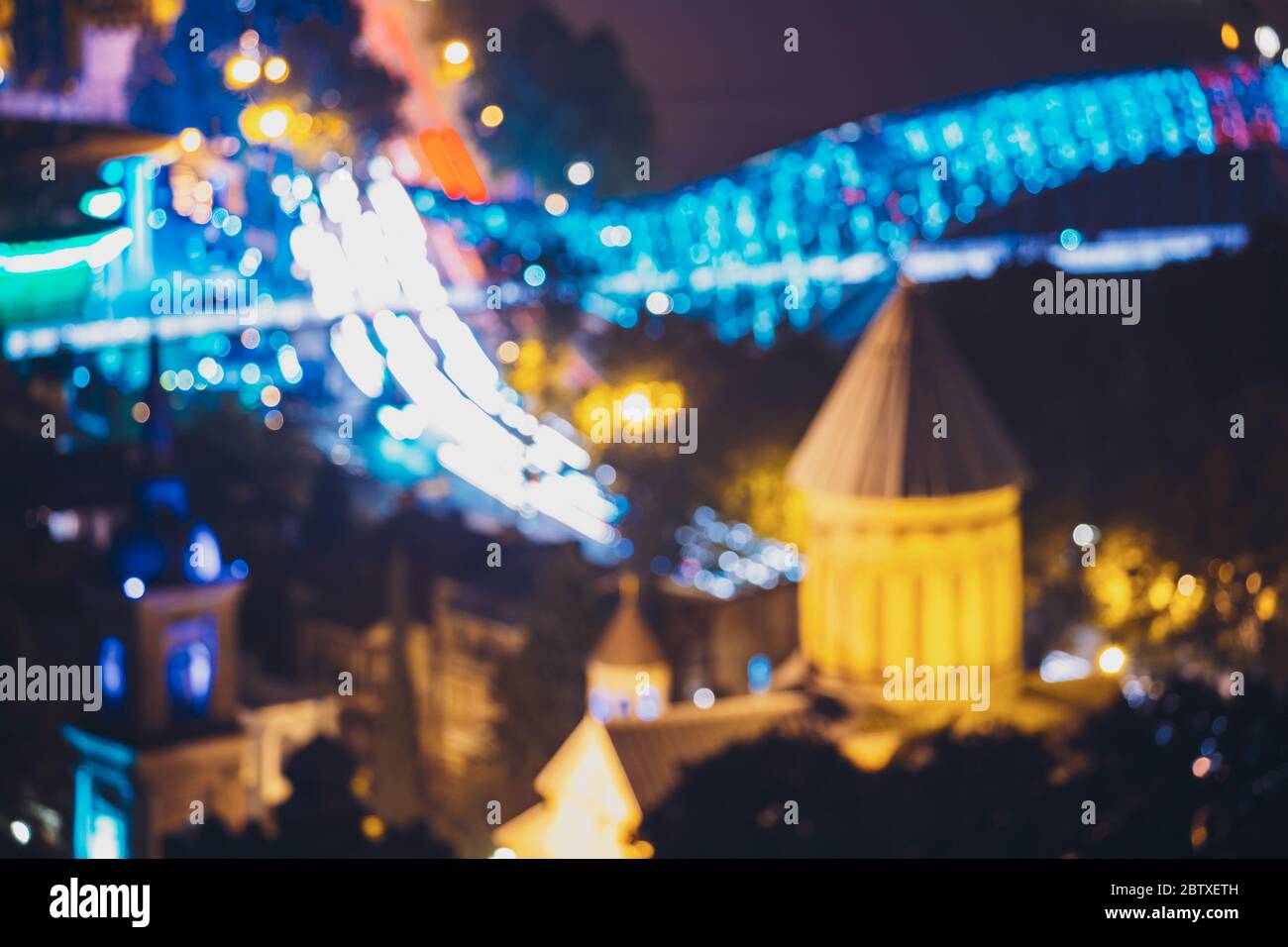 Tbilisi, Georgia. Abstract Blurred Bokeh Architectural Urban sfondo della Cattedrale di Sioni e Ponte della Pace alla sera illuminazione di strada notturna. REA Foto Stock