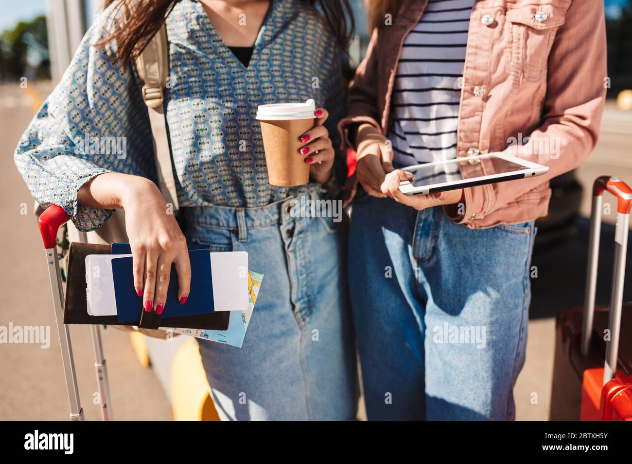 Primo piano ragazze con valigie che tengono caffè per andare, passaporti con biglietti e il tablet in mani in aeroporto Foto Stock
