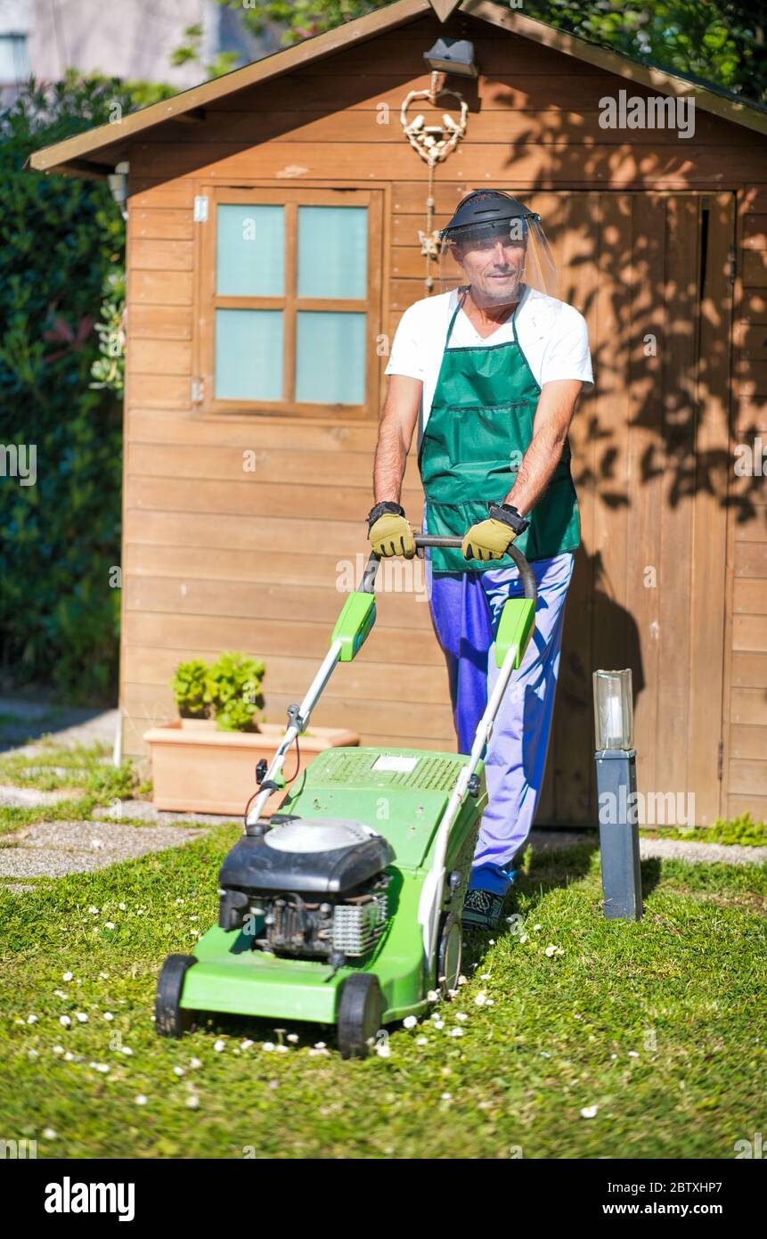 Buon giardiniere maschile che indossa casco utilizzando il rasaerba. Foto Stock