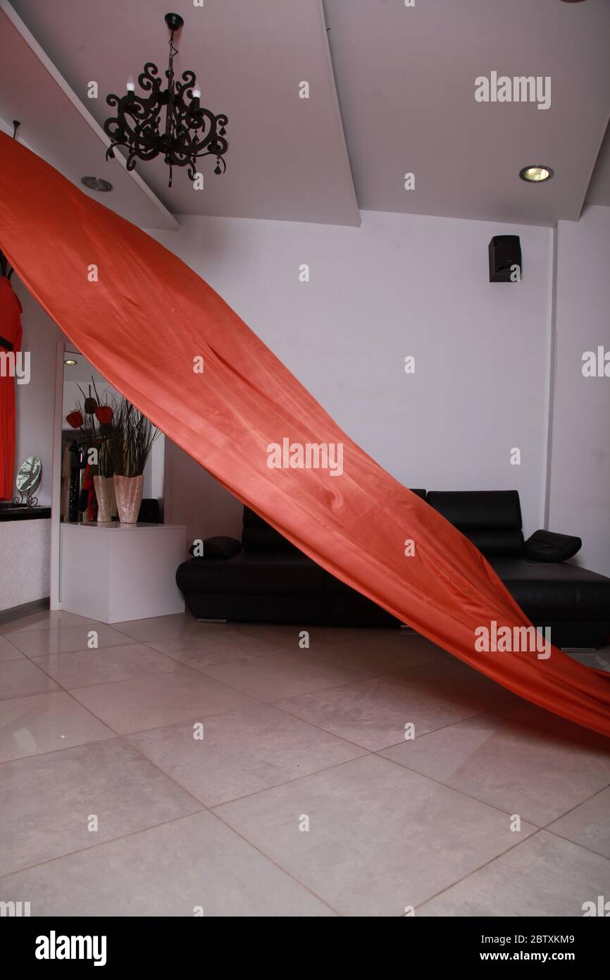 Tessuto di seta arancione che si sfuggono in un interno spazioso con pareti bianche e divano nero, nessuna gente. Foto Stock