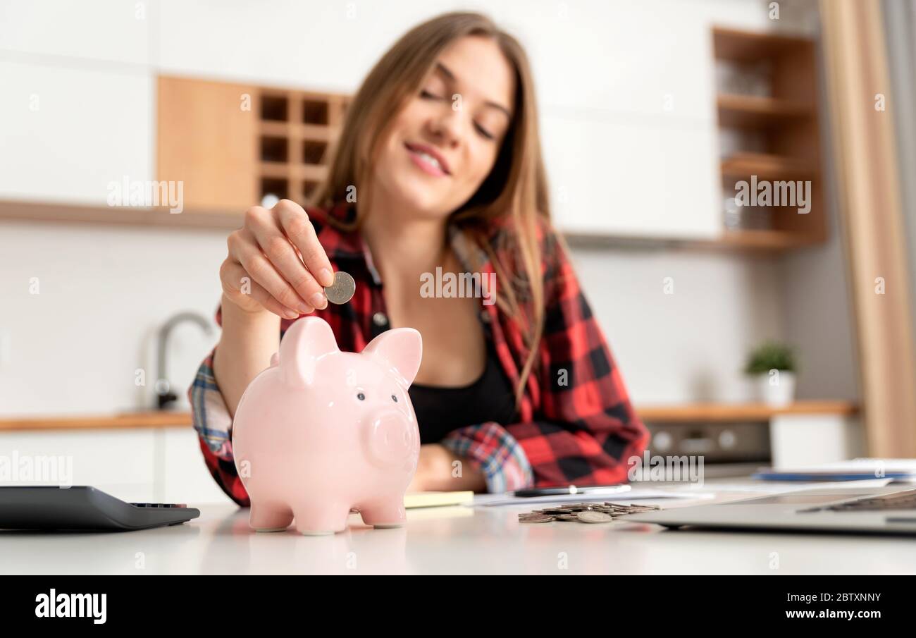 Donna che mette i soldi in banca piggy al tavolo. Concetto di budget domestico Foto Stock