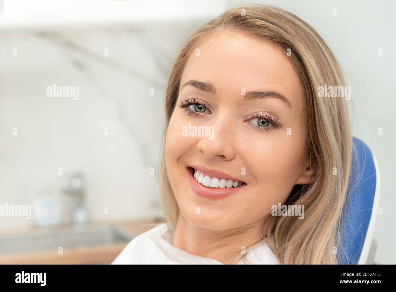 Giovane donna sorridente seduta sulla sedia presso l'ufficio dentista. Cura dentale, denti sani. Foto Stock