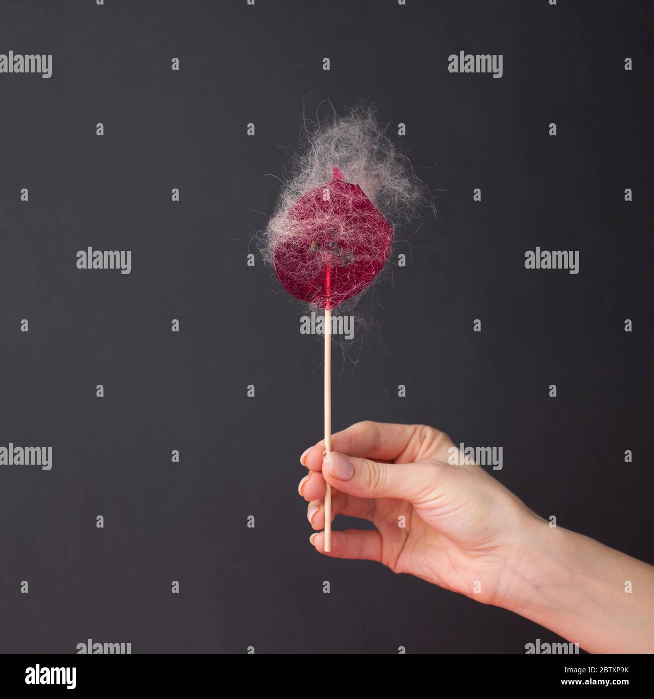Lollipop rosa con capelli appiccicosi in una mano femminile su sfondo nero. Il concetto di salone di bellezza, epilazione, depilazione. Depilazione di cera, sugosa Foto Stock