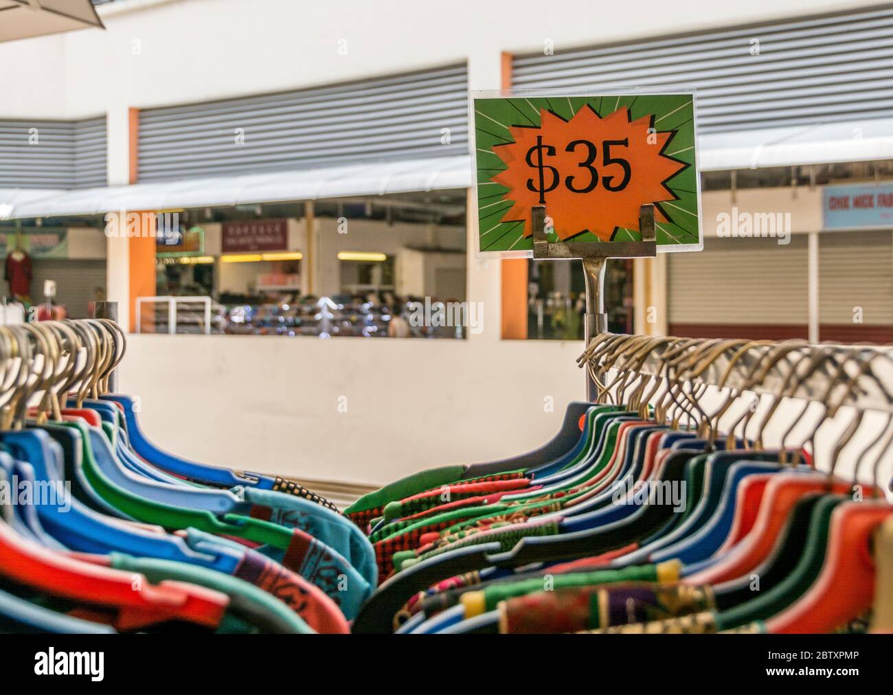 Un segno chiaro, che fa pubblicità al prezzo di vendita di un rack di vestiti su appendiabiti molto colorati Foto Stock