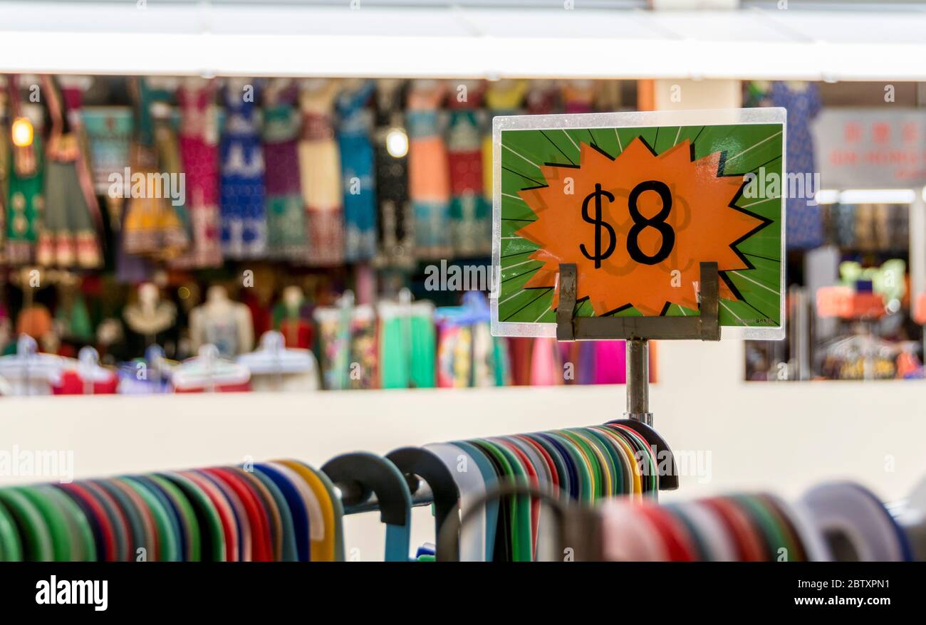 Un segno chiaro, che fa pubblicità al prezzo di vendita di un rack di vestiti su appendiabiti molto colorati Foto Stock