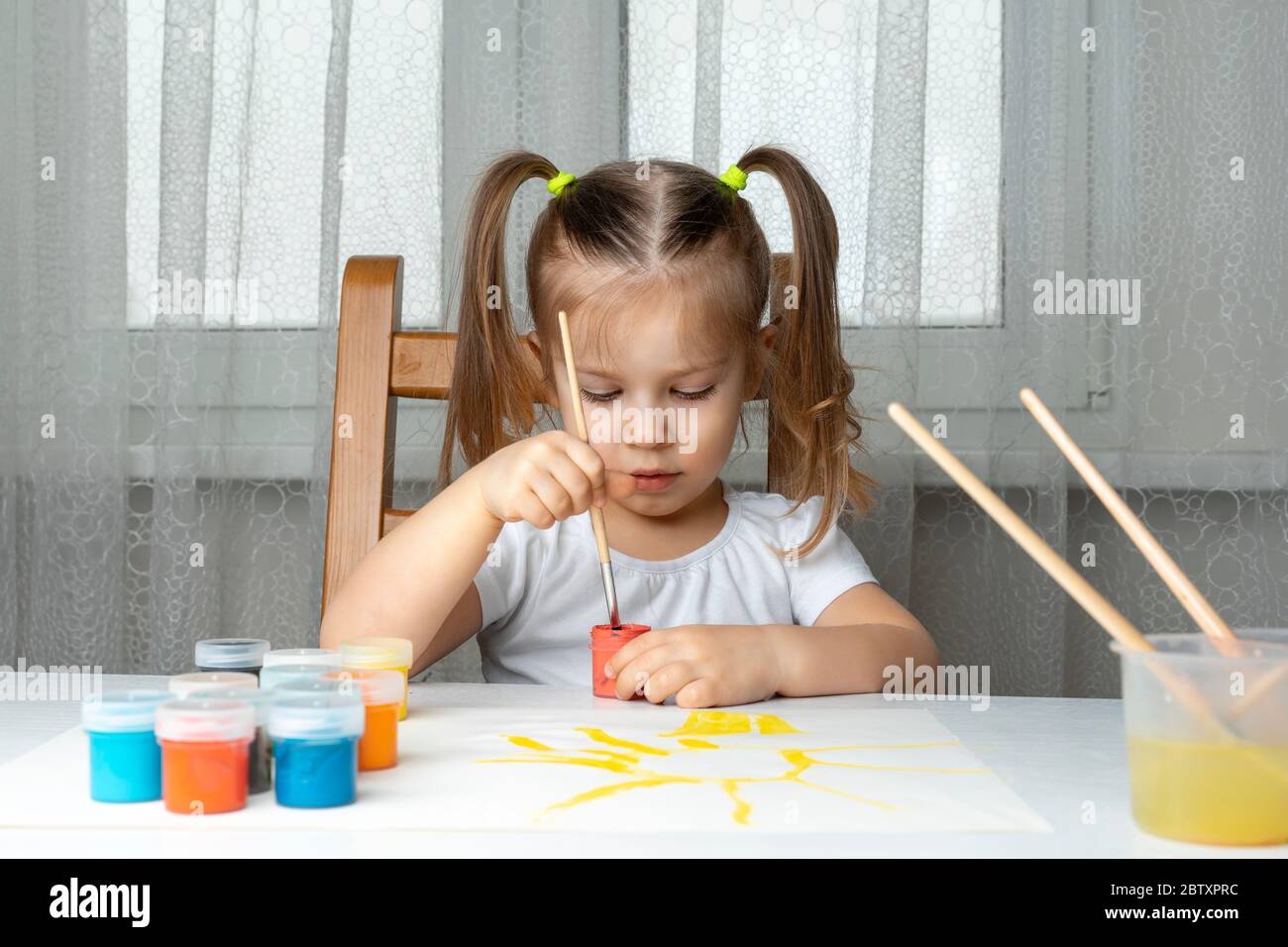 che cosa fare al bambino durante il periodo di quarantena e di auto-isolamento, la ragazza gioca e dipinge. siede e dabs un pennello in un vaso di vernice rossa Foto Stock
