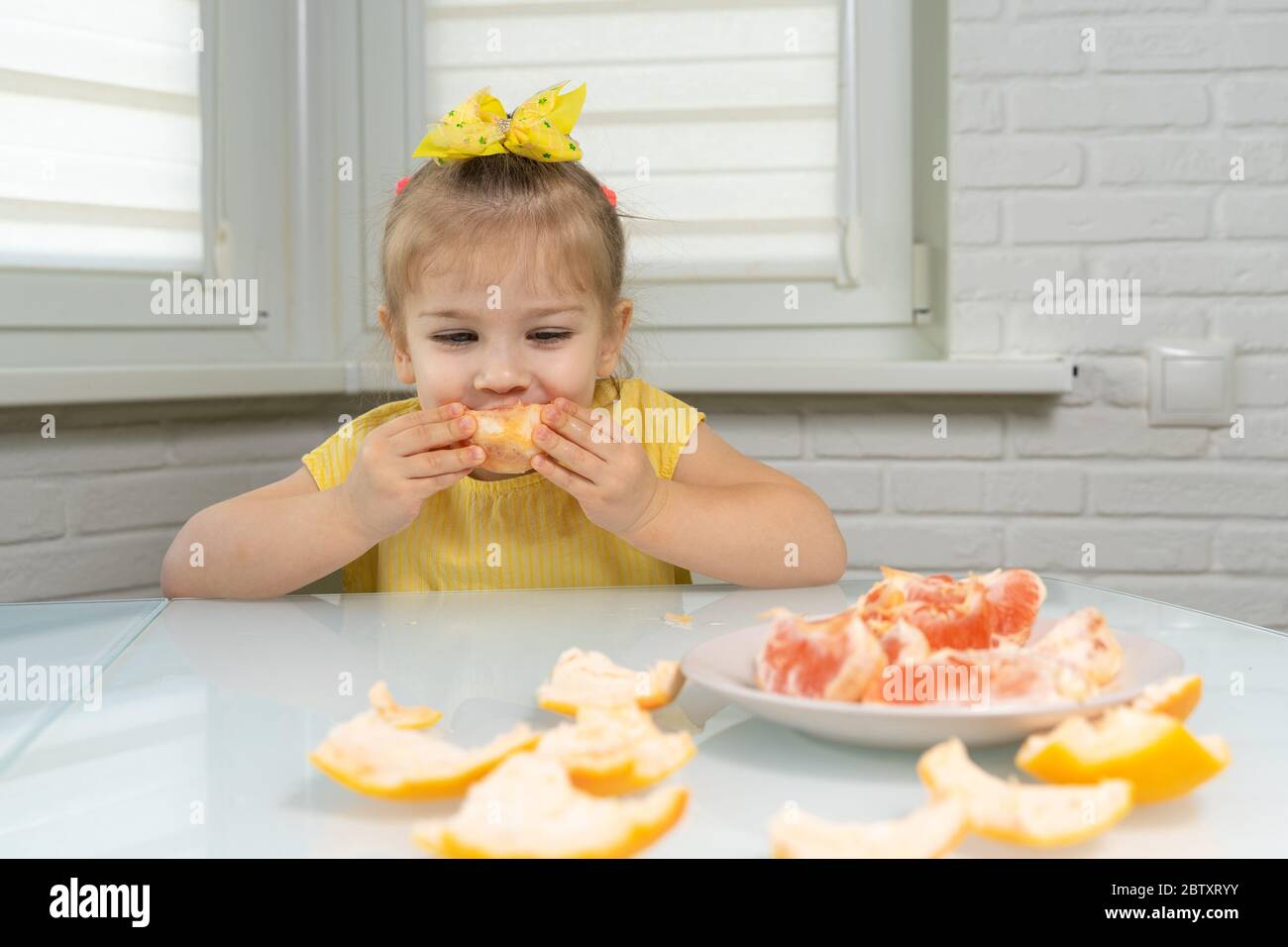 4 anni bambina in una blusa gialla mangia pompelmo con piacere Foto Stock