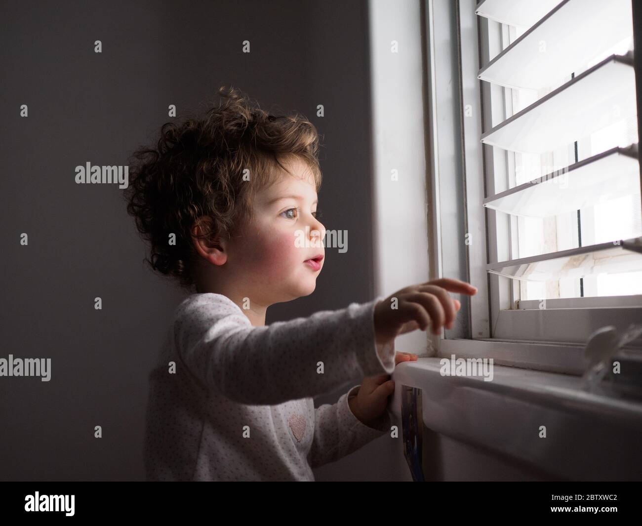 Il bambino di due anni guarda fuori dalla finestra Foto Stock