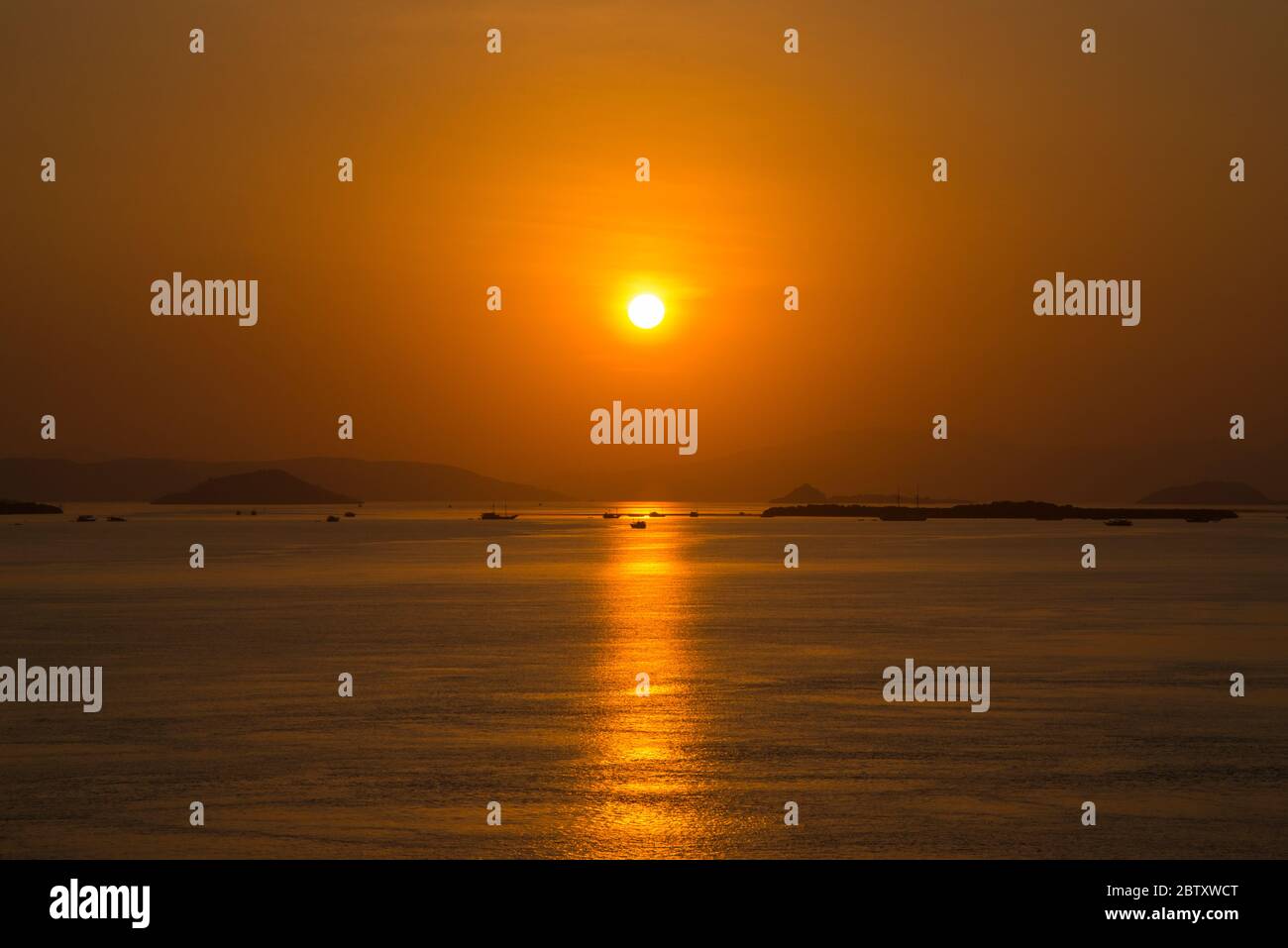 Uno splendido tramonto sul mare al Parco Nazionale di Komodo, Indonesia, con isole e barche sullo sfondo lontano. Foto Stock