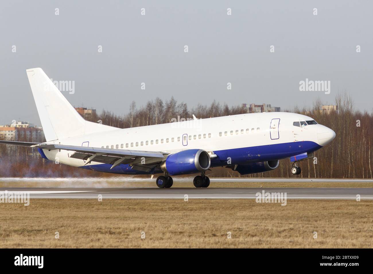 Atterraggio aereo sulla pista all'aeroporto con fumo dal telaio, alberi sullo sfondo. Touchdown con fumo degli pneumatici. Vacanza, viaggio, aviazione Foto Stock