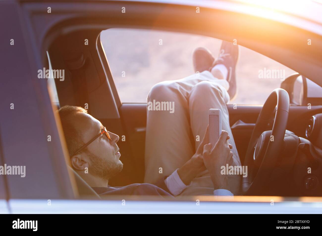 Piedi fuori dalla finestra al tramonto. Uomo conducente messo piedi sulla porta dell'auto, rilassante, godendo di una calda serata estiva, sentire l'aria, fermato a riposare dopo d Foto Stock