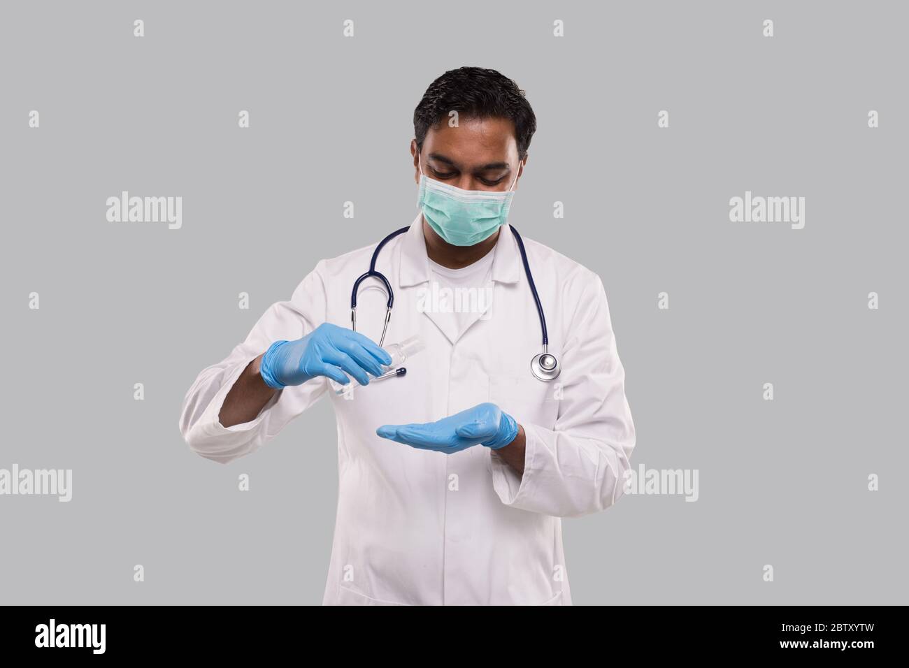 Medico che usa lo sterilizzatore per le mani che indossa maschera medica e guanti. Indiano uomo medico tenendo mani lavano antisettico. Concetto di virus corona. Isolato Foto Stock