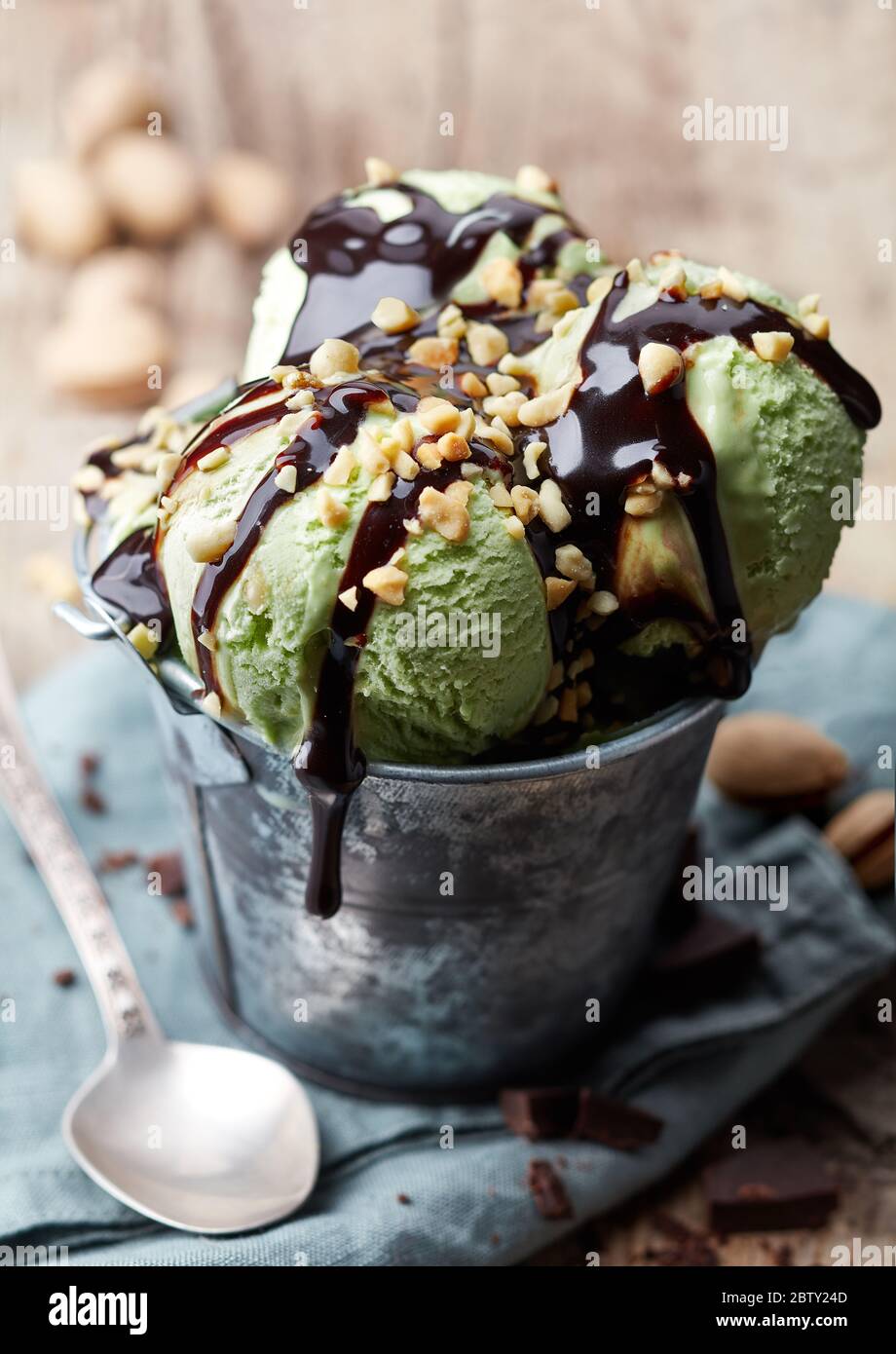 Secchio di gelato al pistacchio verde con salsa al cioccolato e noci su fondo di legno Foto Stock